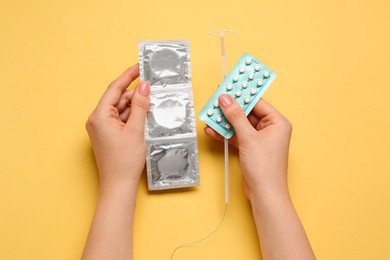 Photo of Woman with condoms, contraceptive pills and intrauterine device on yellow background, top view. Choosing birth control method