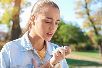 Young woman using asthma inhaler outdoors. Space for text