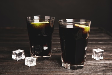 Photo of Refreshing soda drinks with ice cubes and lime on black wooden table