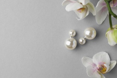 Elegant pearl earrings and orchid flowers on white background, flat lay. Space for text