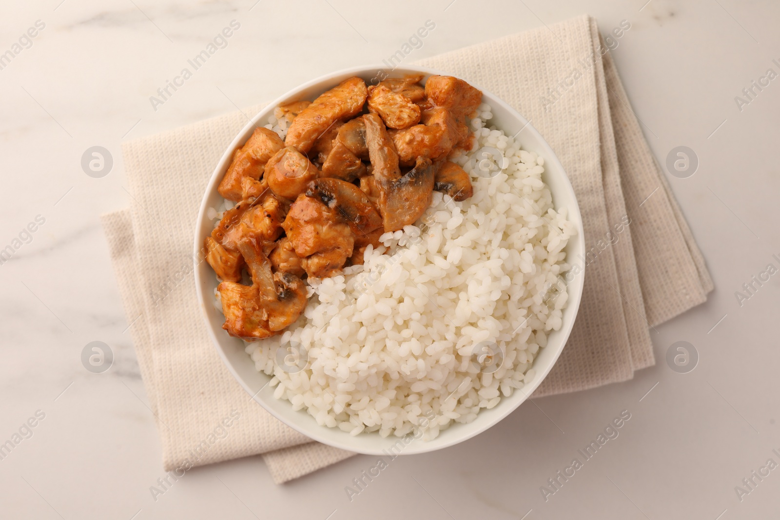 Photo of Bowl of delicious rice with meat and mushrooms on white marble table, top view