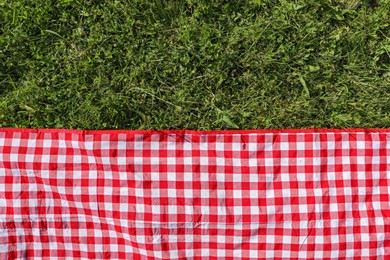 Checkered picnic tablecloth on fresh green grass, top view. Space for text