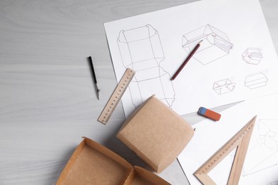 Photo of Creating packaging design. Drawings, boxes and stationery on light wooden table, flat lay