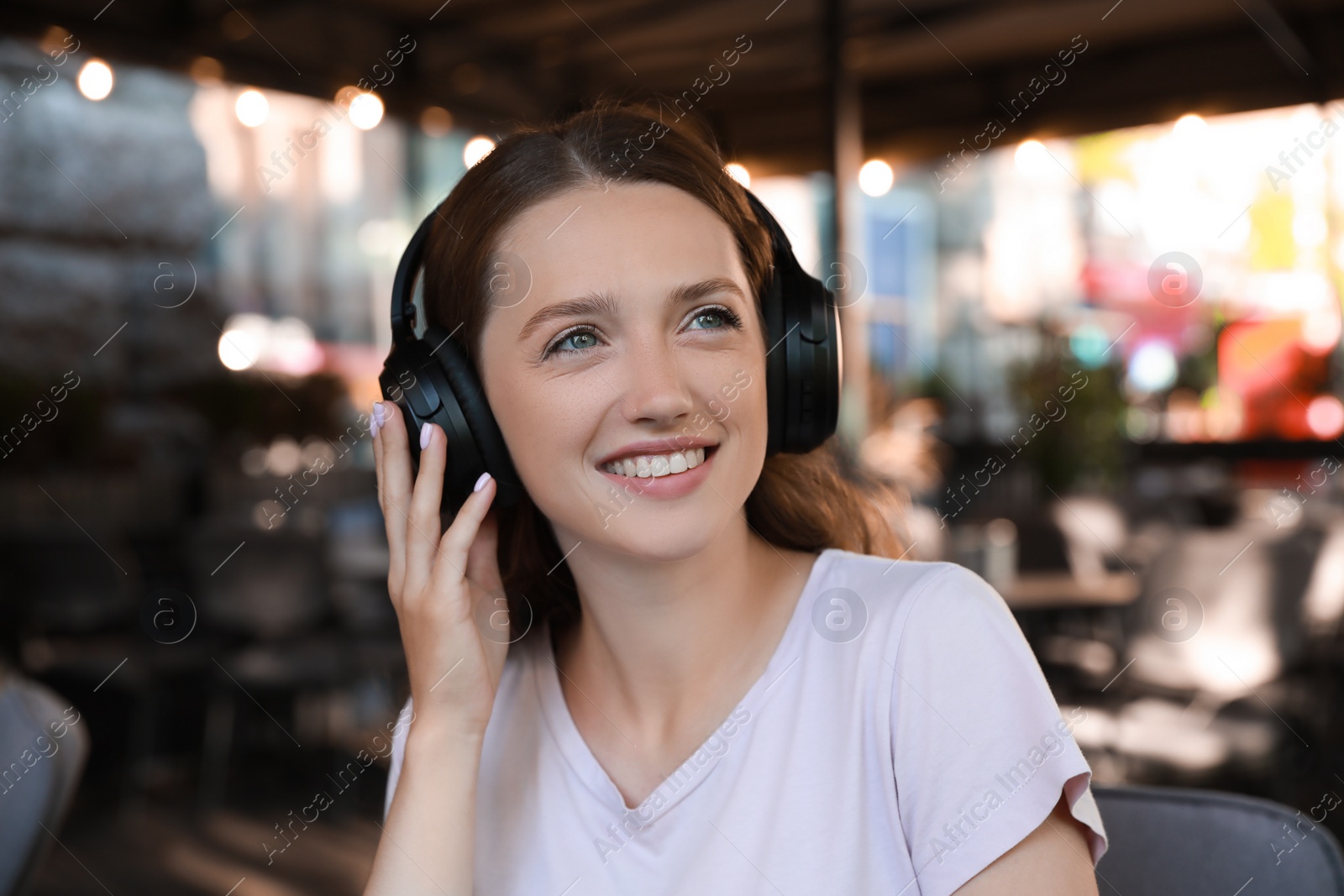 Photo of Smiling woman in headphones listening to music in outdoor cafe