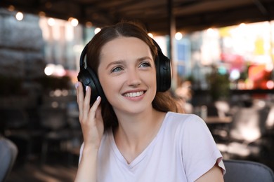 Smiling woman in headphones listening to music in outdoor cafe