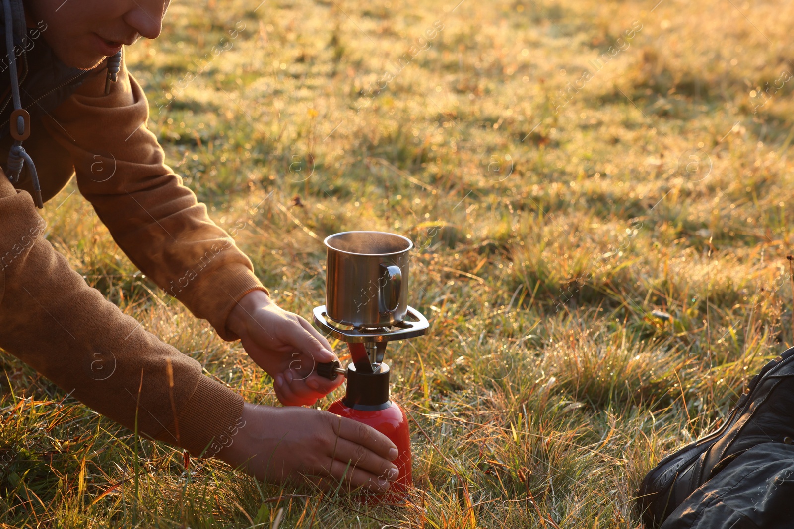 Photo of Tourist making hot drink with camping burner outdoors, closeup. Space for text