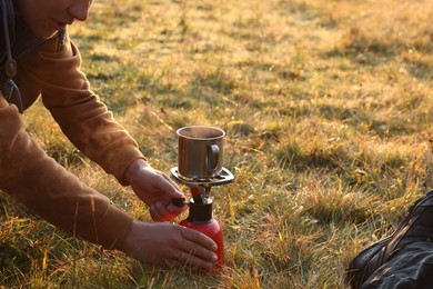 Photo of Tourist making hot drink with camping burner outdoors, closeup. Space for text