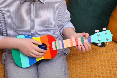 Photo of Woman playing ukulele on sofa at home, closeup