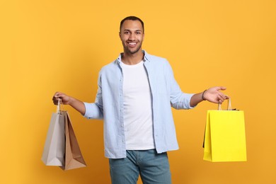 Happy African American man with shopping bags on orange background