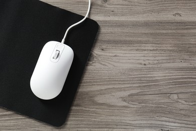 Photo of Wired mouse and mousepad on wooden table, top view. Space for text