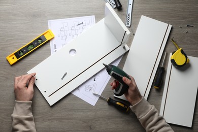 Photo of Man with electric screwdriver assembling white furniture at table, top view