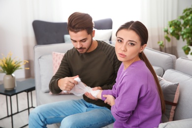 Photo of Young man applying bandage on woman's injured hand at home. First aid