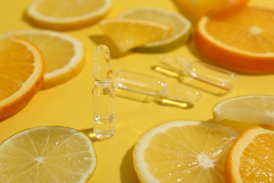 Skincare ampoules with vitamin C and citrus slices on yellow background, closeup