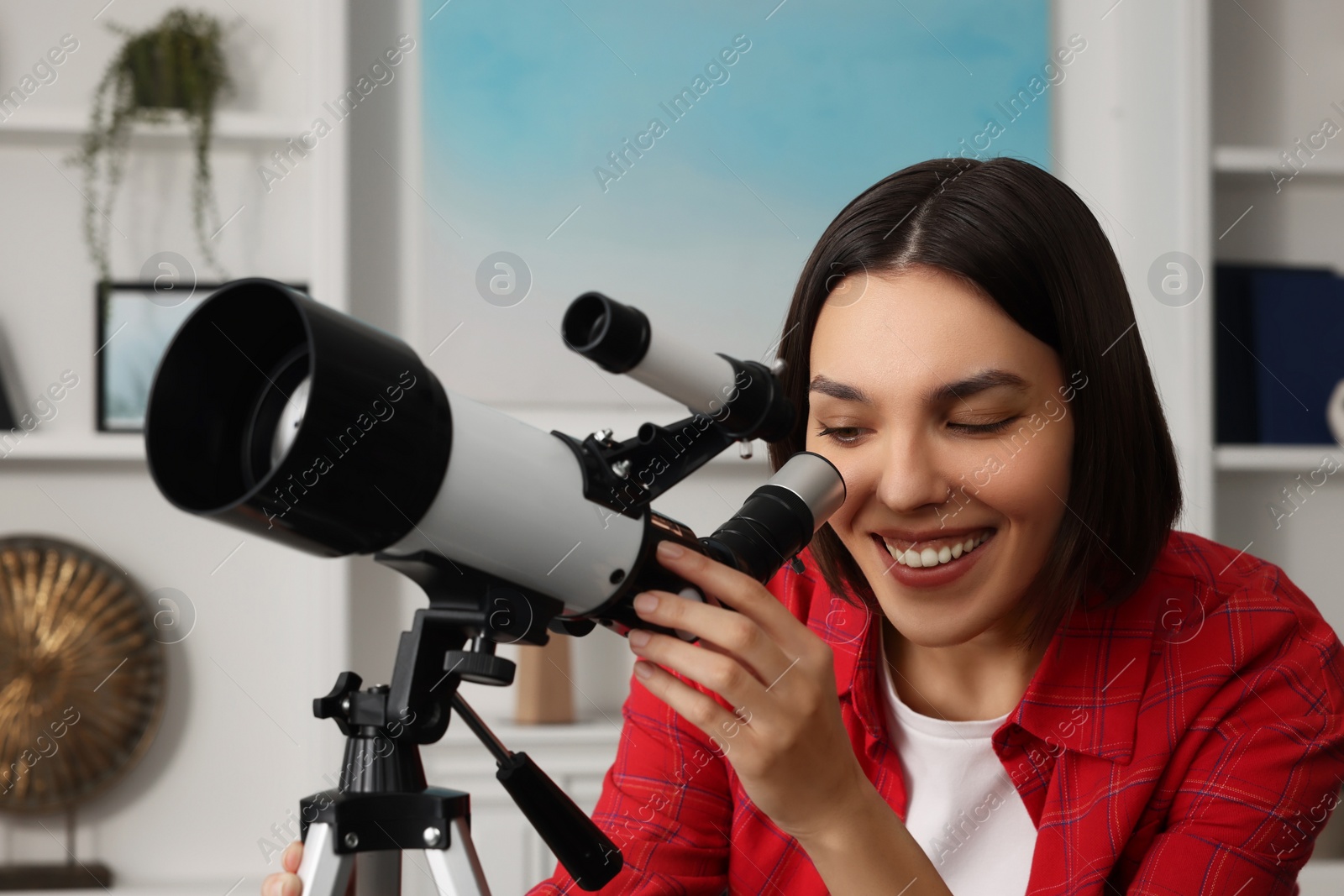 Photo of Beautiful young woman looking at stars through telescope in room