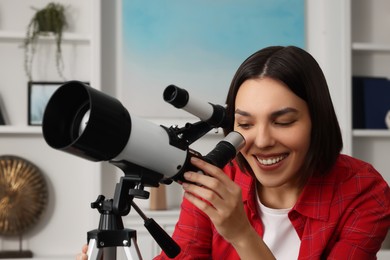 Photo of Beautiful young woman looking at stars through telescope in room