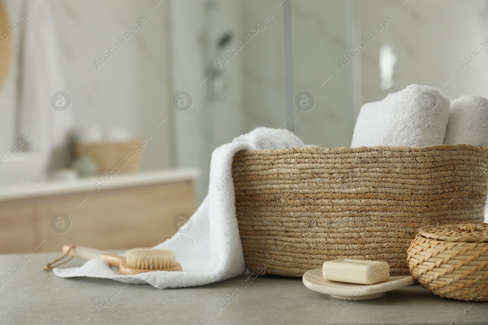 Photo of Wicker basket with clean towels and massage brush on table in bathroom