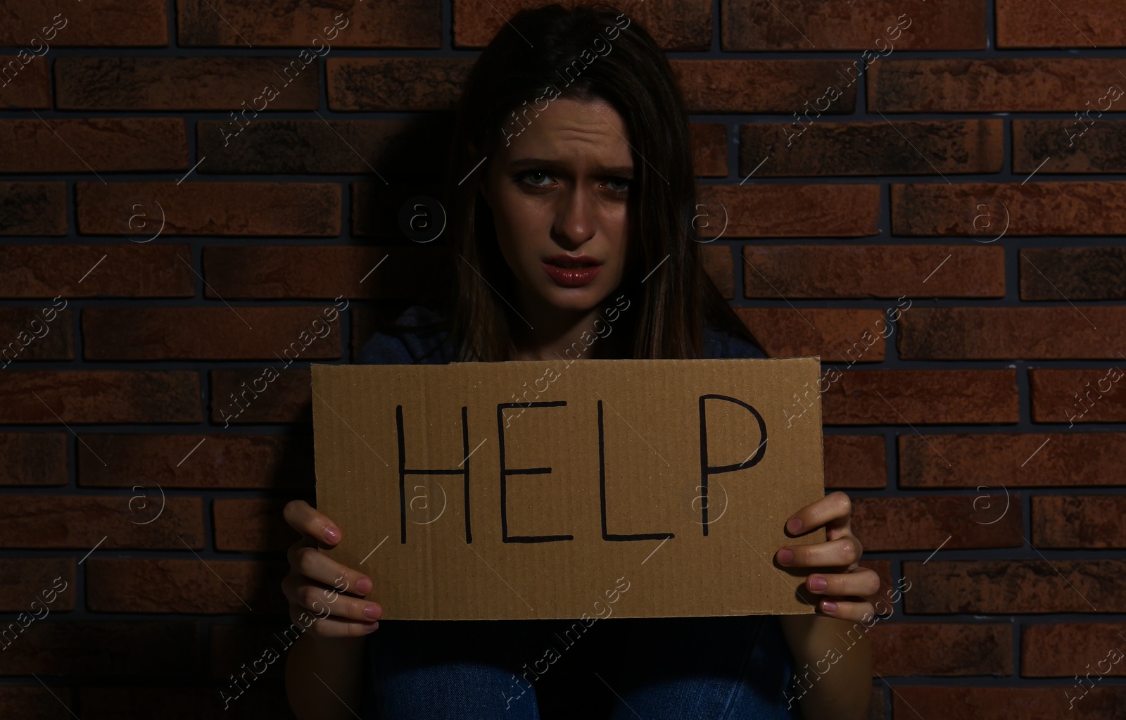 Photo of Abused young woman with sign HELP near brick wall. Domestic violence concept