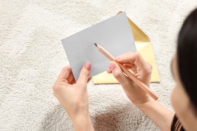 Photo of Woman writing message in greeting card on carpet in room, closeup