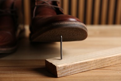 Metal nail in wooden plank and shoes on table, closeup