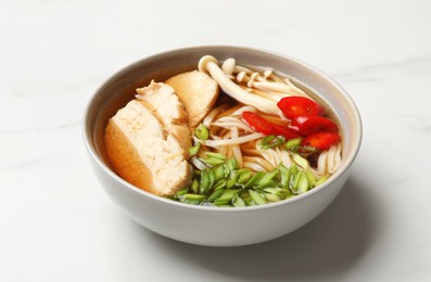 Photo of Delicious ramen with meat and mushrooms in bowl on white marble table. Noodle soup