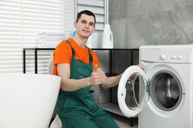 Photo of Smiling plumber showing thumb up near washing machine in bathroom