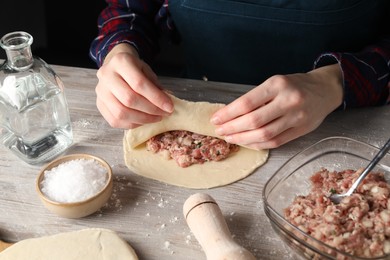 Photo of Woman making chebureki with meat at wooden table, closeup