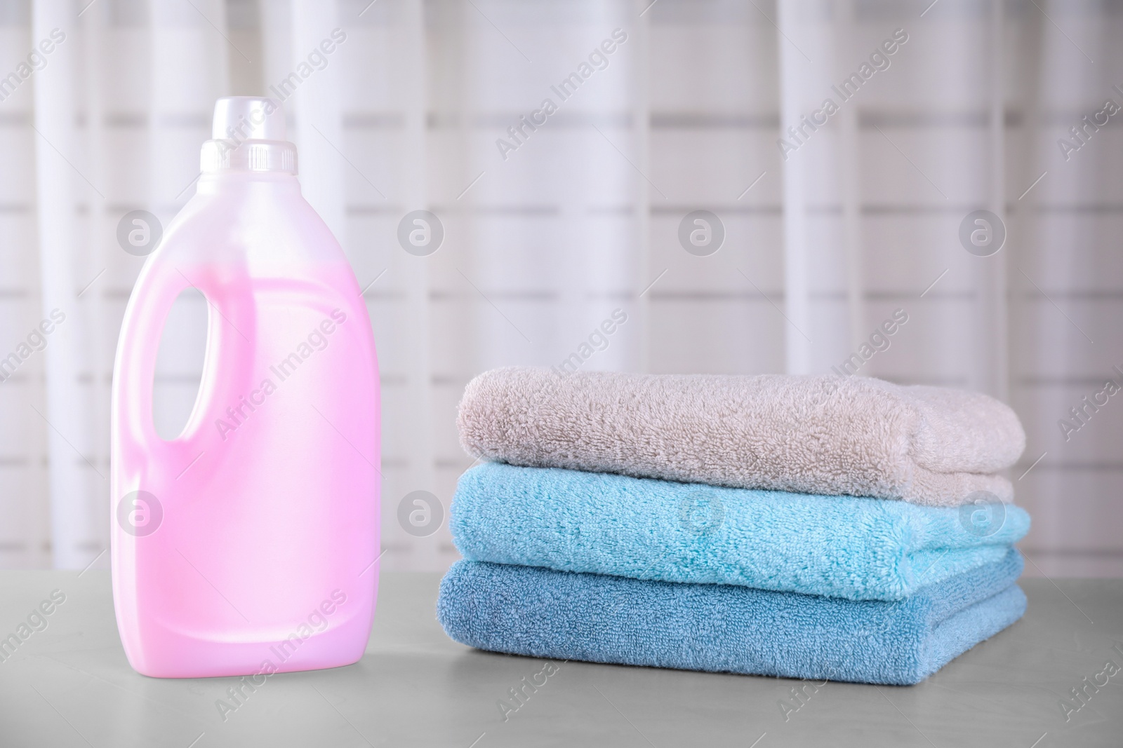 Photo of Clean towels and bottle of laundry detergent on table against blurred background