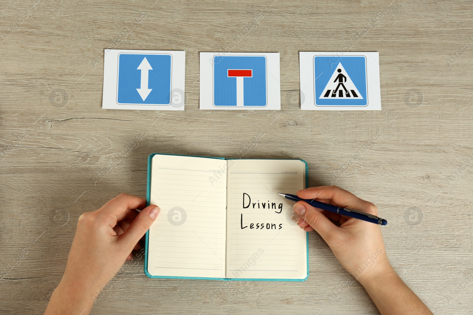 Photo of Woman with workbook for driving lessons and road signs at wooden table, top view. Passing license exam