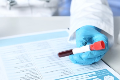 Photo of Specialist holding sample tube near laboratory test form medical on table, closeup. Research and analysis