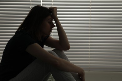 Photo of Sad young woman near window indoors, space for text