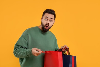 Excited man with many paper shopping bags on orange background