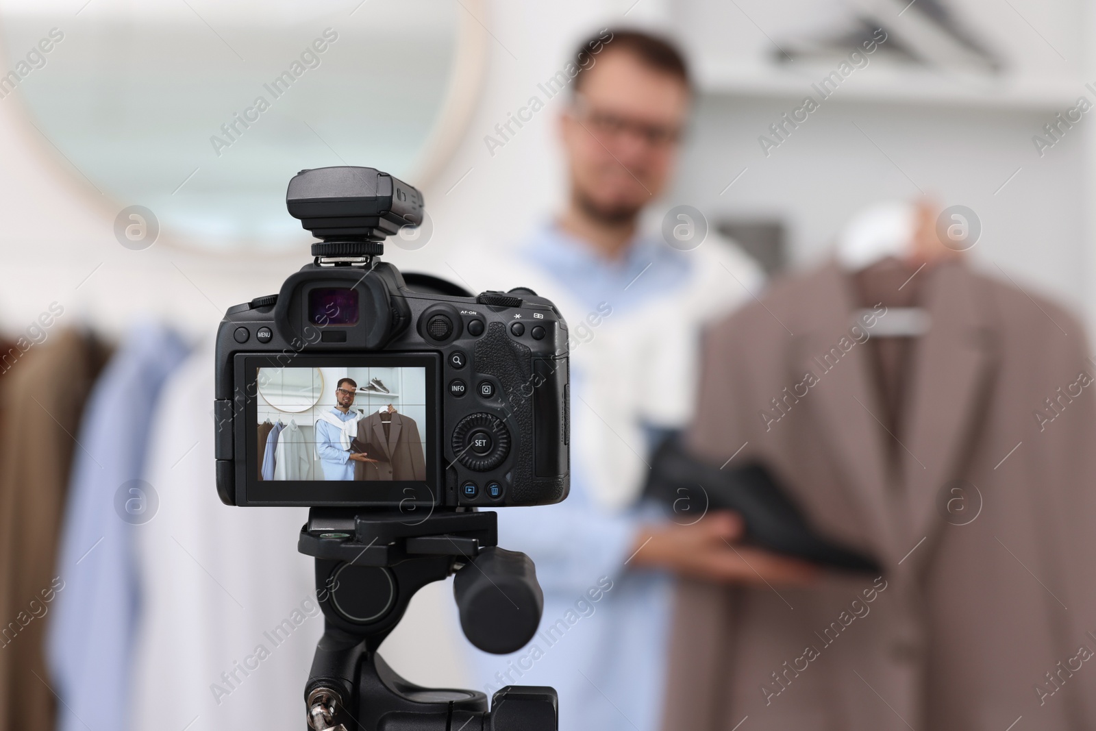 Photo of Fashion blogger showing clothes while recording video at home, focus on camera