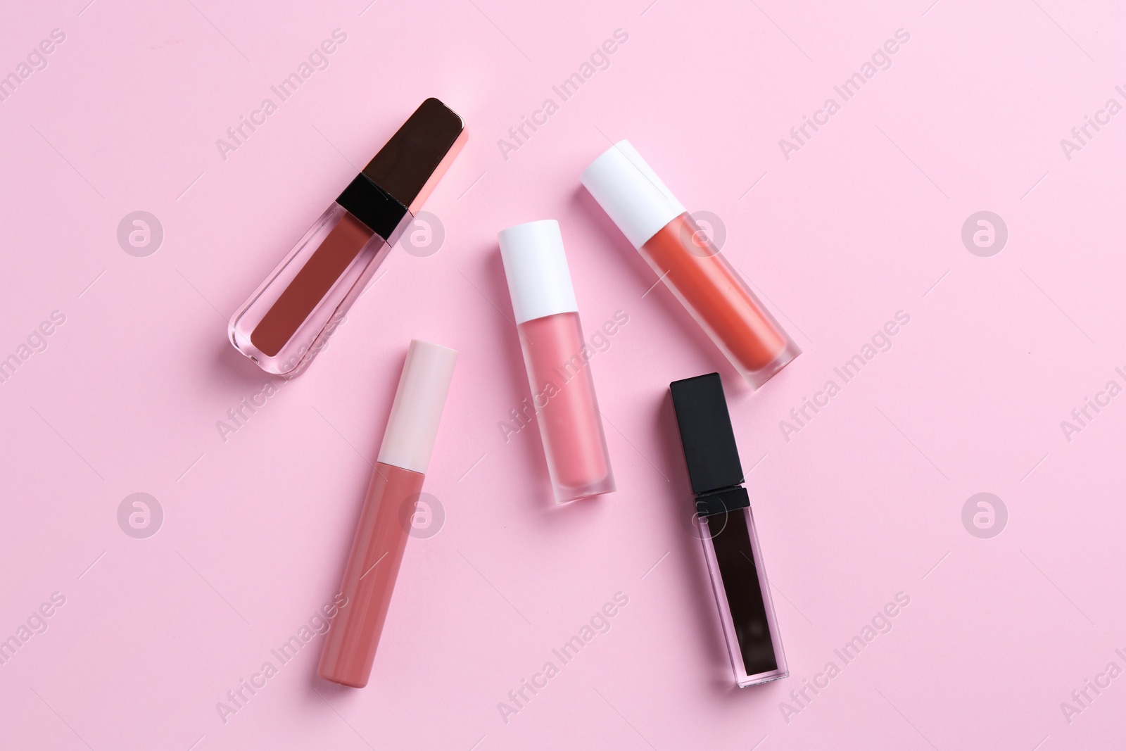 Photo of Different lip glosses on pink background, flat lay