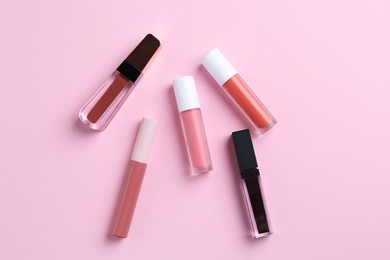 Photo of Different lip glosses on pink background, flat lay