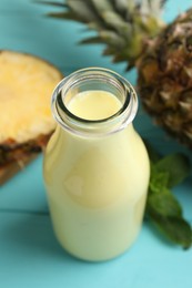 Tasty pineapple smoothie in bottle, mint and fruit on light blue wooden table, closeup