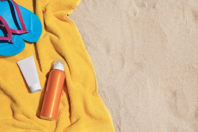 Photo of Sunscreens, flip flops and towel on sand, top view with space for text. Sun protection care