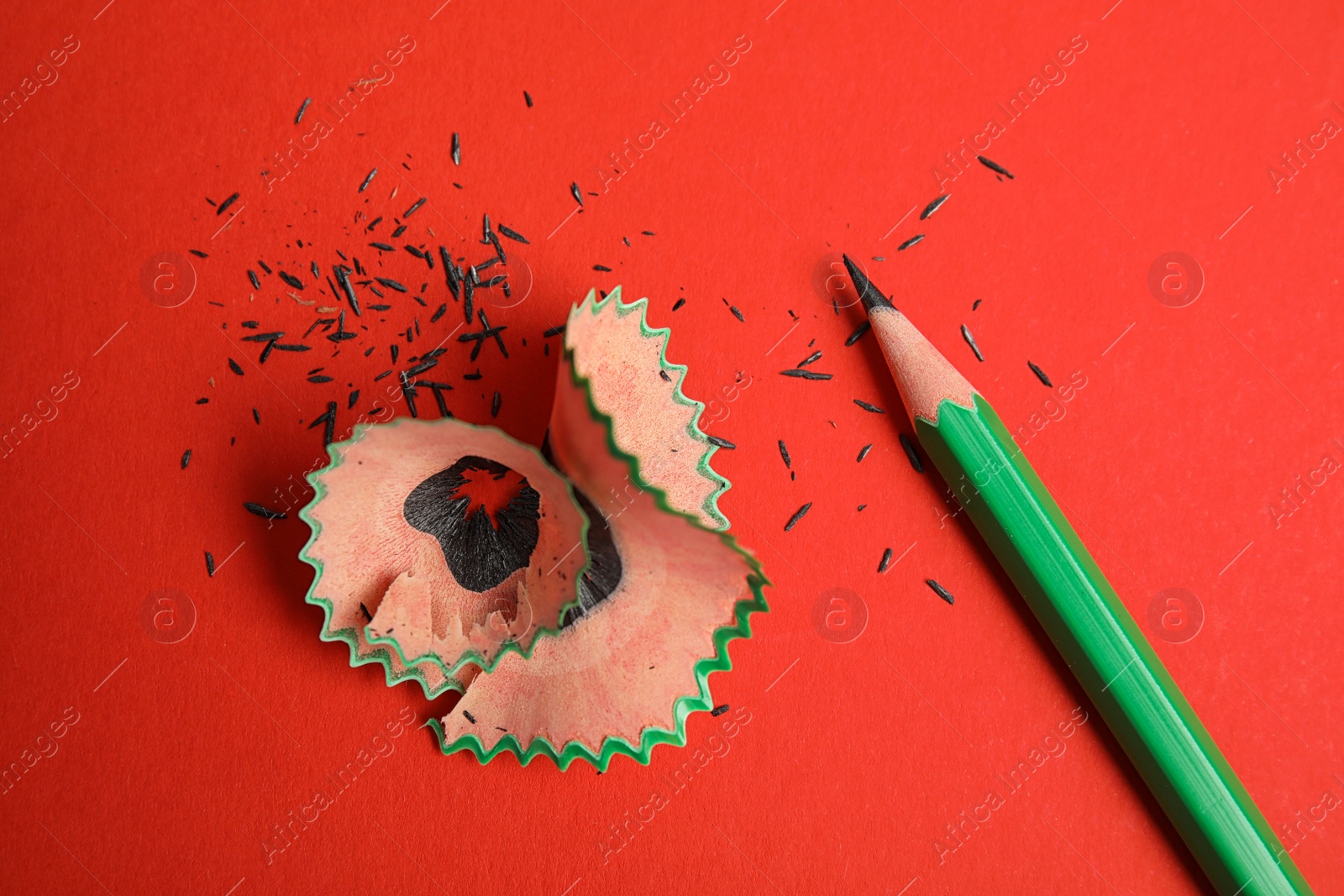 Photo of Pencil and shavings on red background, above view