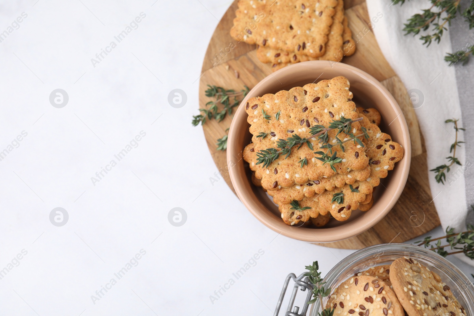 Photo of Cereal crackers with flax, sesame seeds and thyme in bowl on white table, top view. Space for text