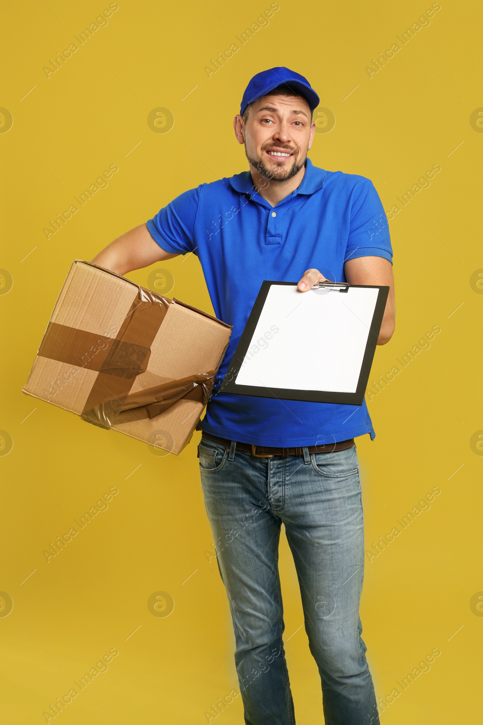 Photo of Emotional courier with damaged cardboard box and clipboard on yellow background. Poor quality delivery service