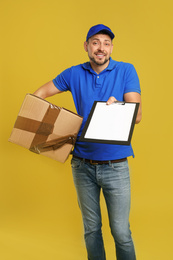 Photo of Emotional courier with damaged cardboard box and clipboard on yellow background. Poor quality delivery service