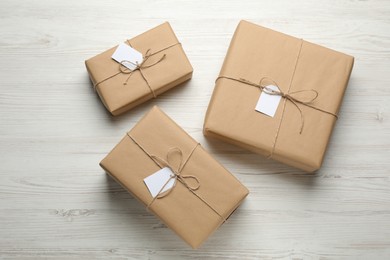 Photo of Parcels wrapped in kraft paper with tags on white wooden table, flat lay