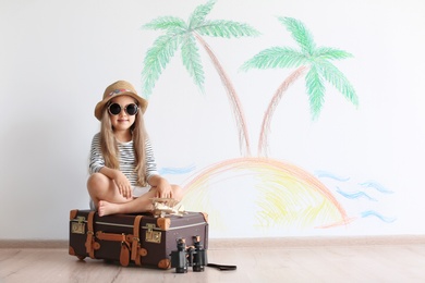 Photo of Adorable little child playing traveler with suitcase indoors