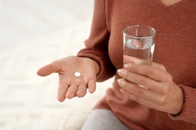 Senior woman with pill and glass of water indoors, closeup