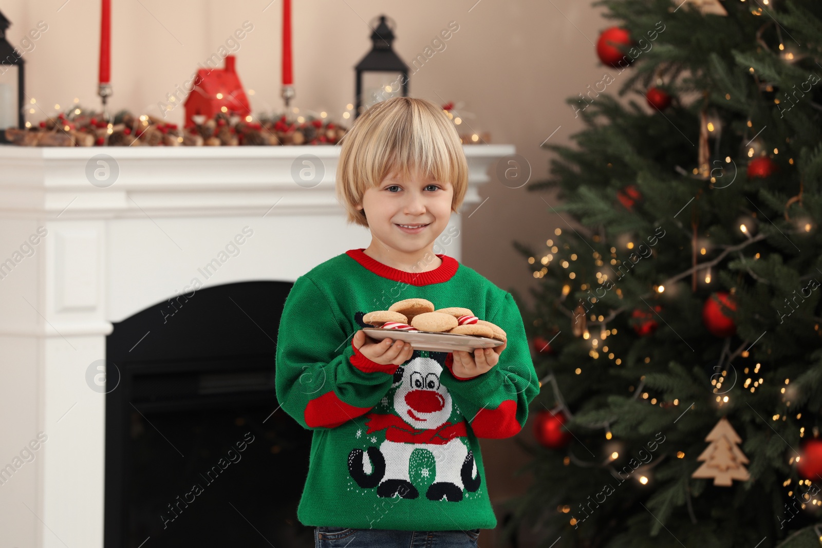 Photo of Little child holding plate of cookies and candy canes at home. Christmas celebration