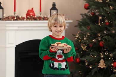 Photo of Little child holding plate of cookies and candy canes at home. Christmas celebration