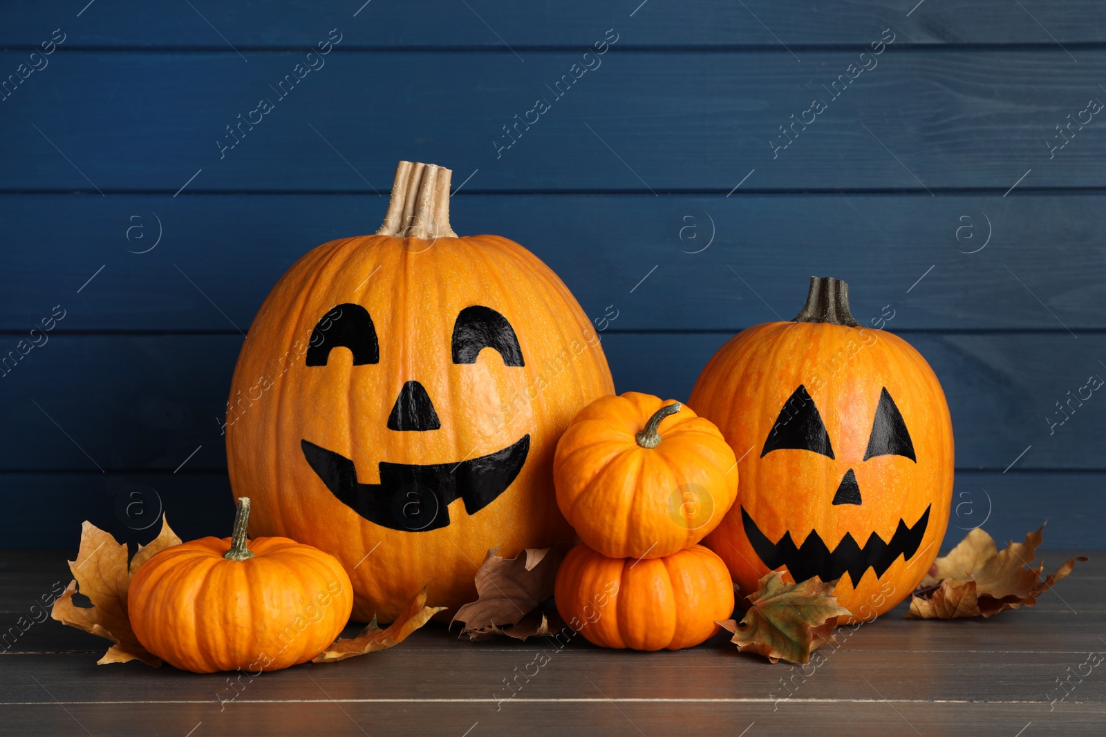 Photo of Orange pumpkins and two with drawn spooky faces on wooden table. Halloween celebration