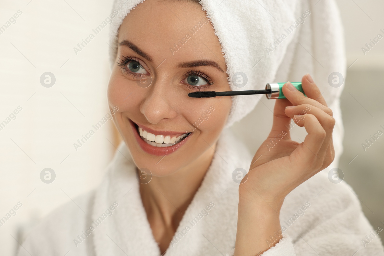 Photo of Beautiful woman applying mascara with brush indoors, closeup