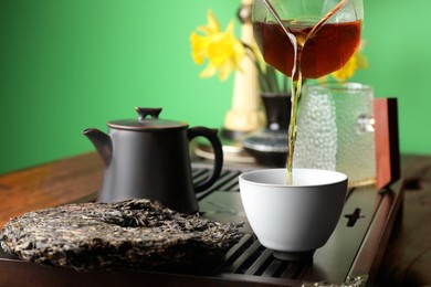 Pouring freshly brewed pu-erh tea into cup on table, closeup