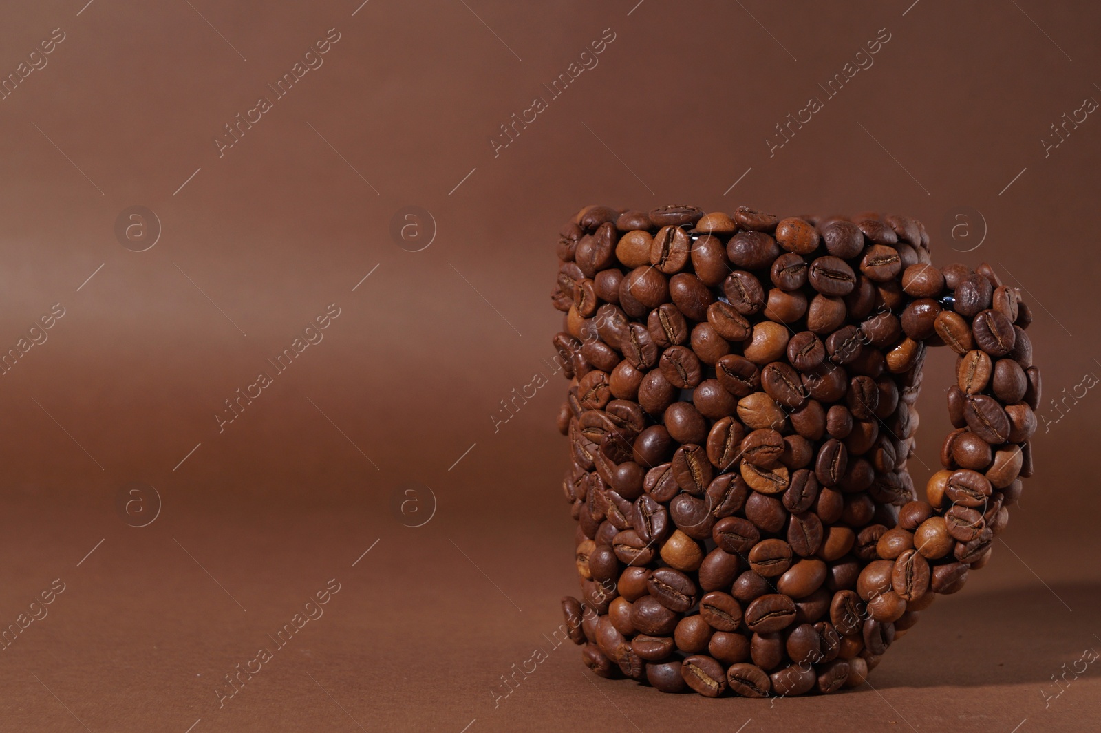 Photo of Cup made of coffee beans on brown background. Space for text