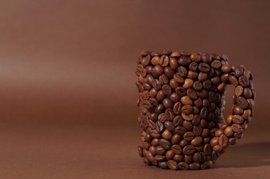 Cup made of coffee beans on brown background. Space for text